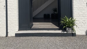 Um edifício de tijolos brancos com uma grande entrada em arco, uma escadaria que leva a um andar superior e duas plantas em vasos na parte externa.