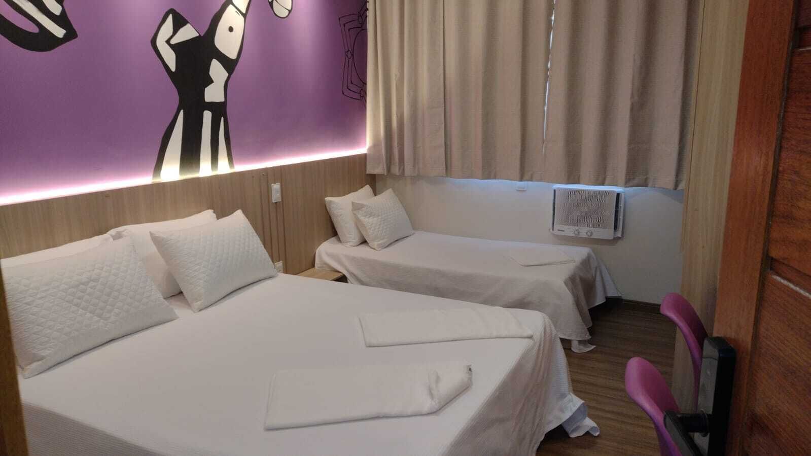 A hotel room with two beds, a wall mural, a window with curtains, and a ceiling fan.