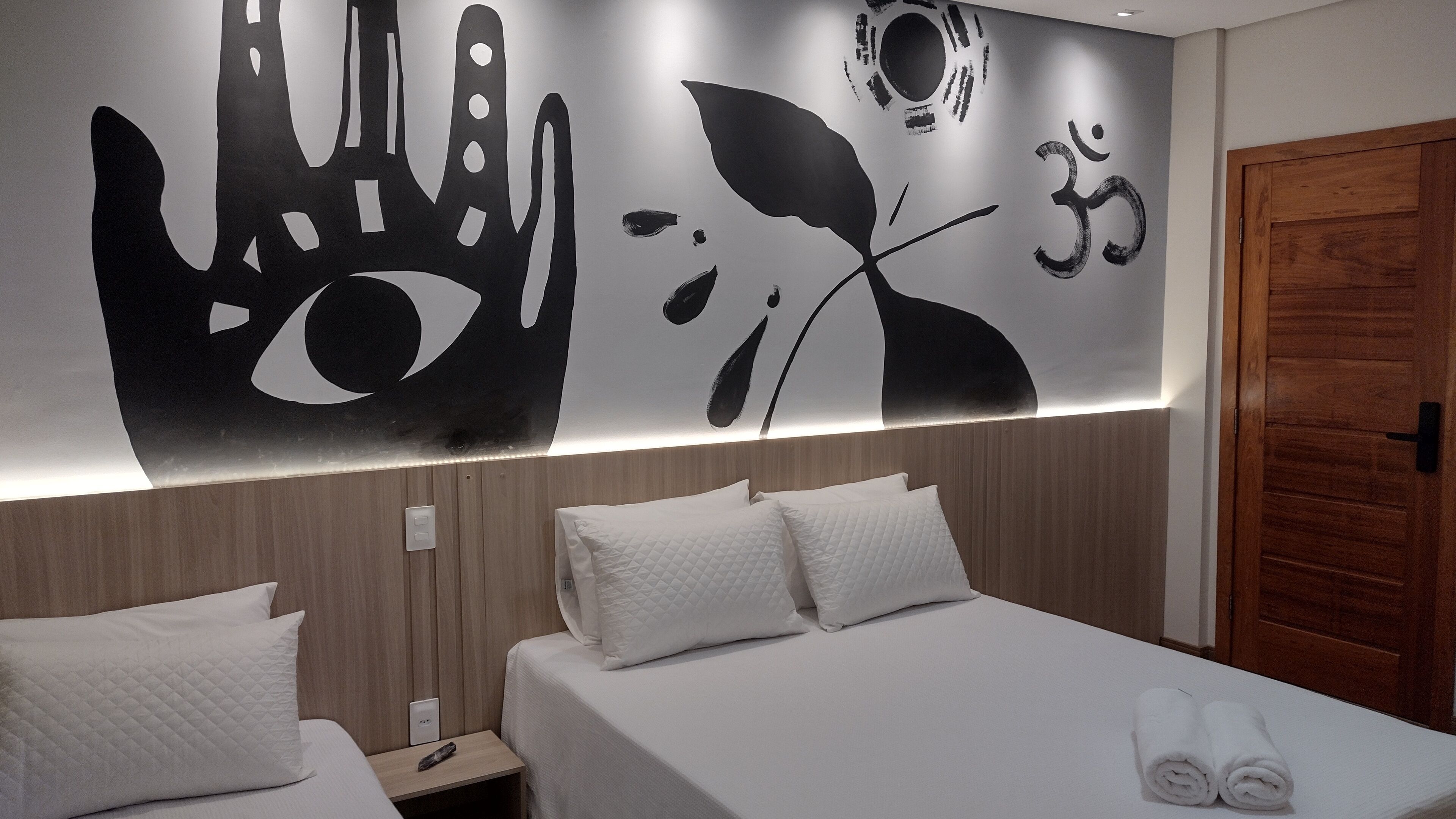 A hotel room with a bed, two pillows, a nightstand, and a wall with a large black and white artwork.