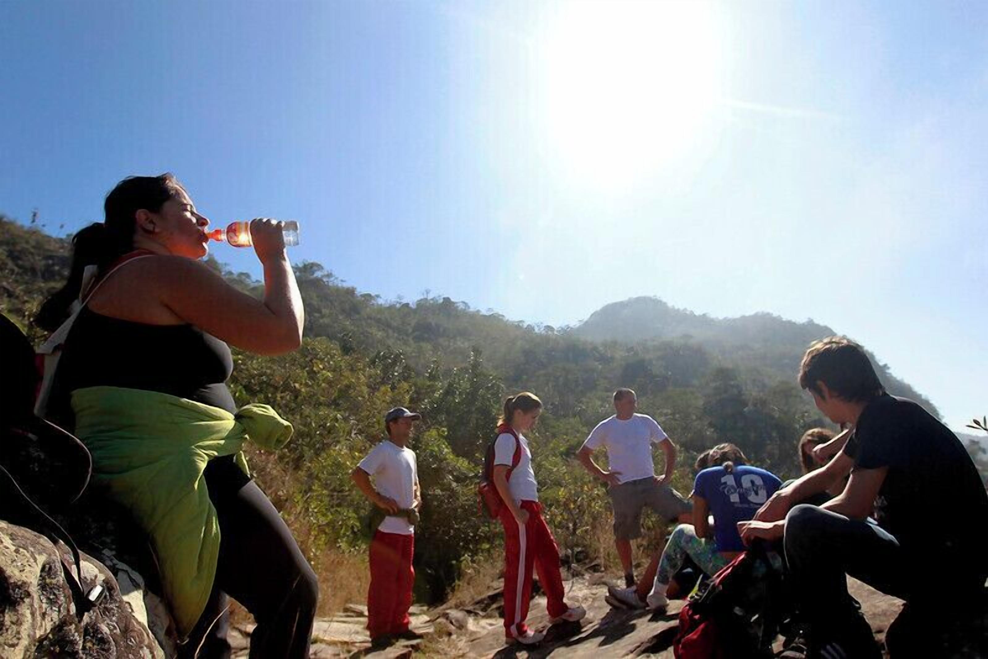 A group of people sitting on a rocky ledge with a mountainous landscape in the background.