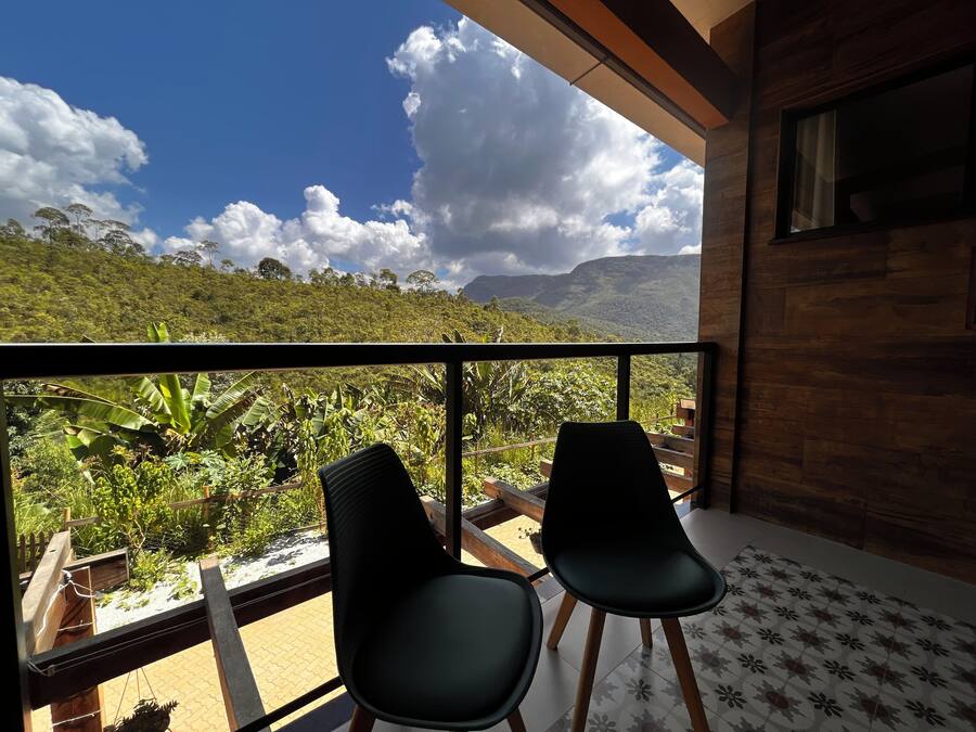 A balcony with two chairs, a view of lush greenery and mountains, and a wooden floor.