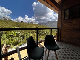 Un balcón con dos sillas, vista a exuberante vegetación y montañas, y piso de madera.