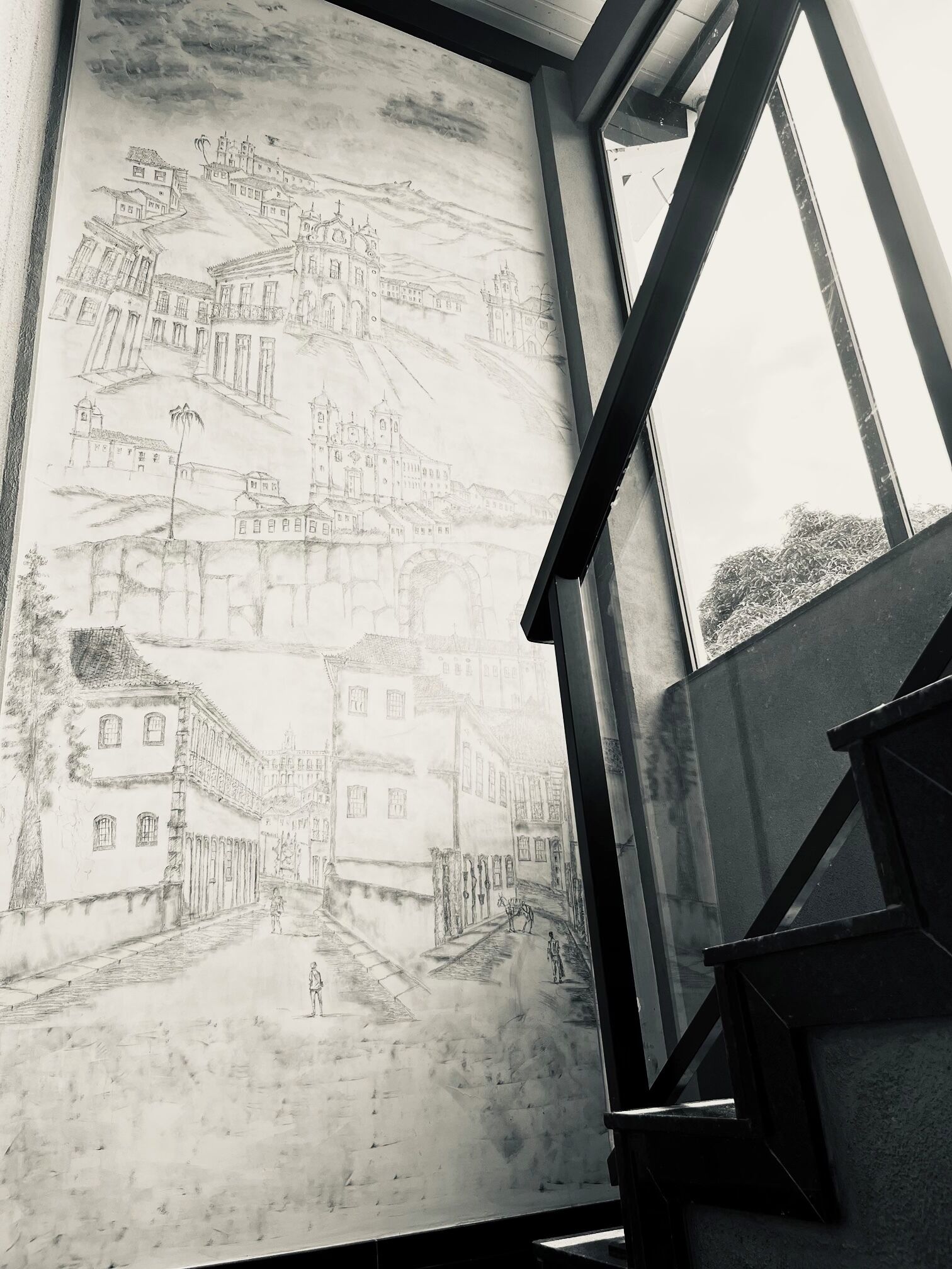 Un gran boceto detallado a lápiz de un pueblo con edificios y una iglesia, expuesto cerca de una ventana.