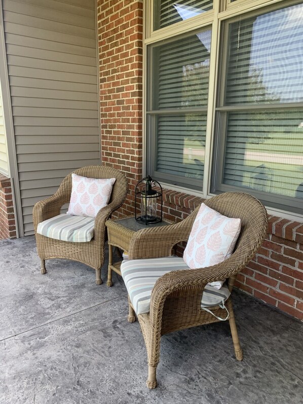 A patio with wicker furniture, including two chairs and a small table, with a lantern on the table.