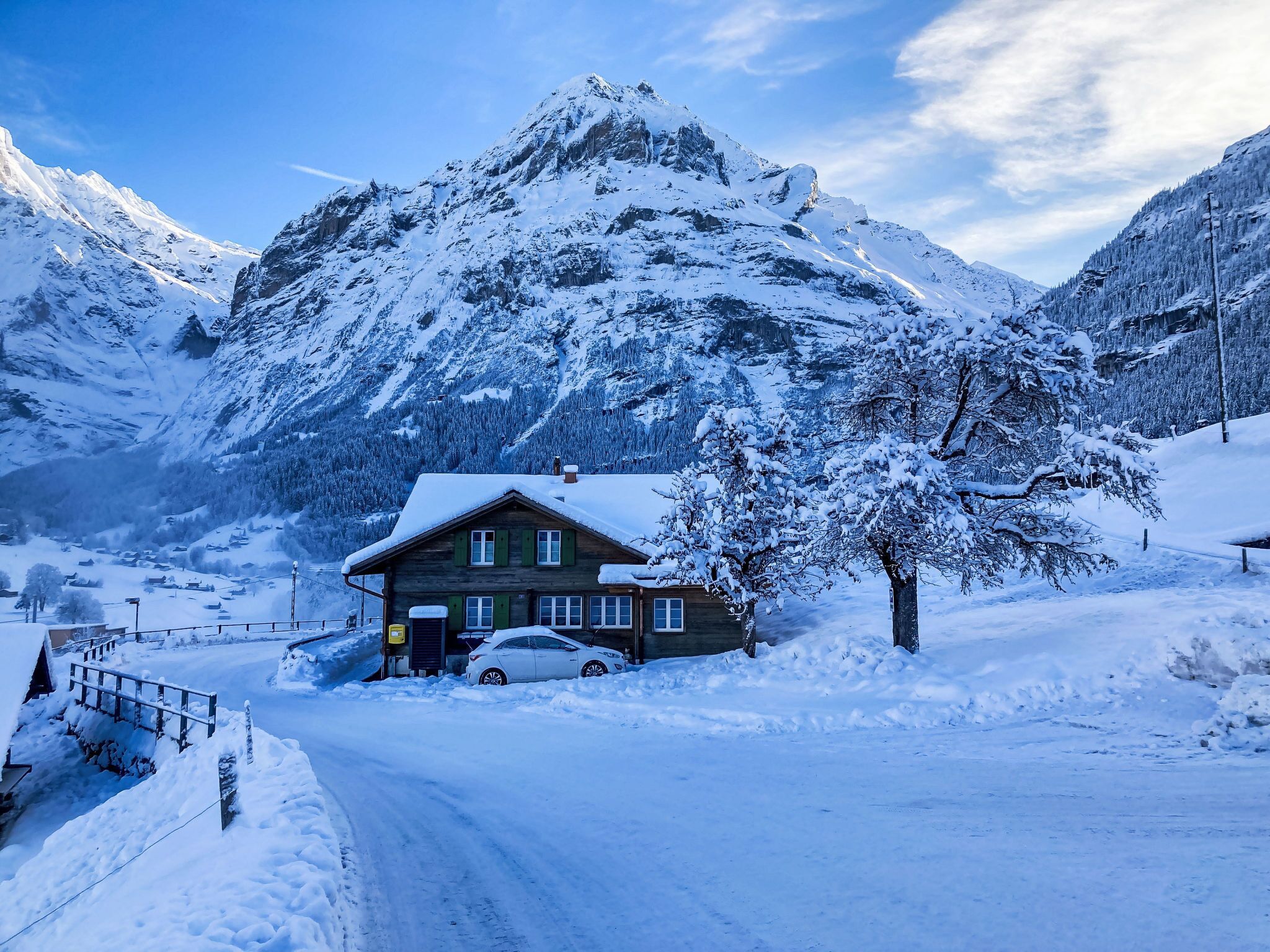 Ein mit Schnee bedeckter Berg, im Vordergrund ein Holzhaus.