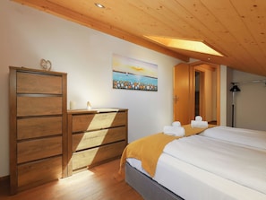 Un dormitorio con un aparador de madera, un cuadro de un atardecer, una cama con sábanas blancas y un tragaluz.