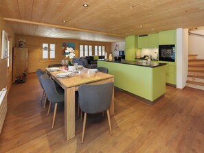 A modern kitchen with green cabinets, a wooden dining table with chairs, and a kitchen island.