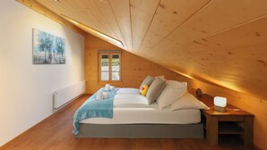 Una camera da letto con soffitto in legno, un letto con cuscini e coperta, un comodino con lampada e una finestra vista.