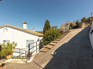 Uma rua residencial com uma casa branca, uma escadaria e um jardim.