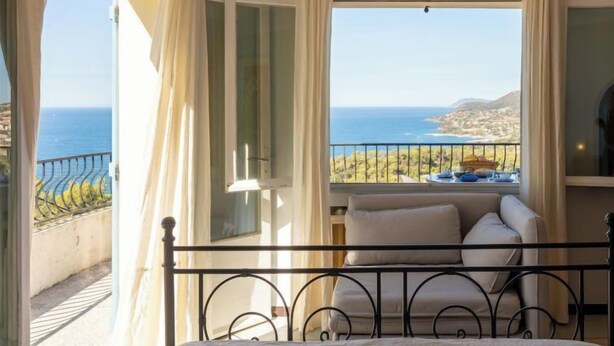 Un dormitorio con cama, vista al mar y balcón con silla y mesa.