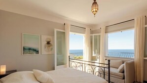 Un dormitorio con una cama grande, un balcón con vistas al mar y obras de arte en las paredes.