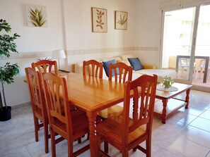A dining area with a wooden table and chairs, a sofa with cushions, and a potted plant on a small table. - Dianium by Interhome (Dénia)