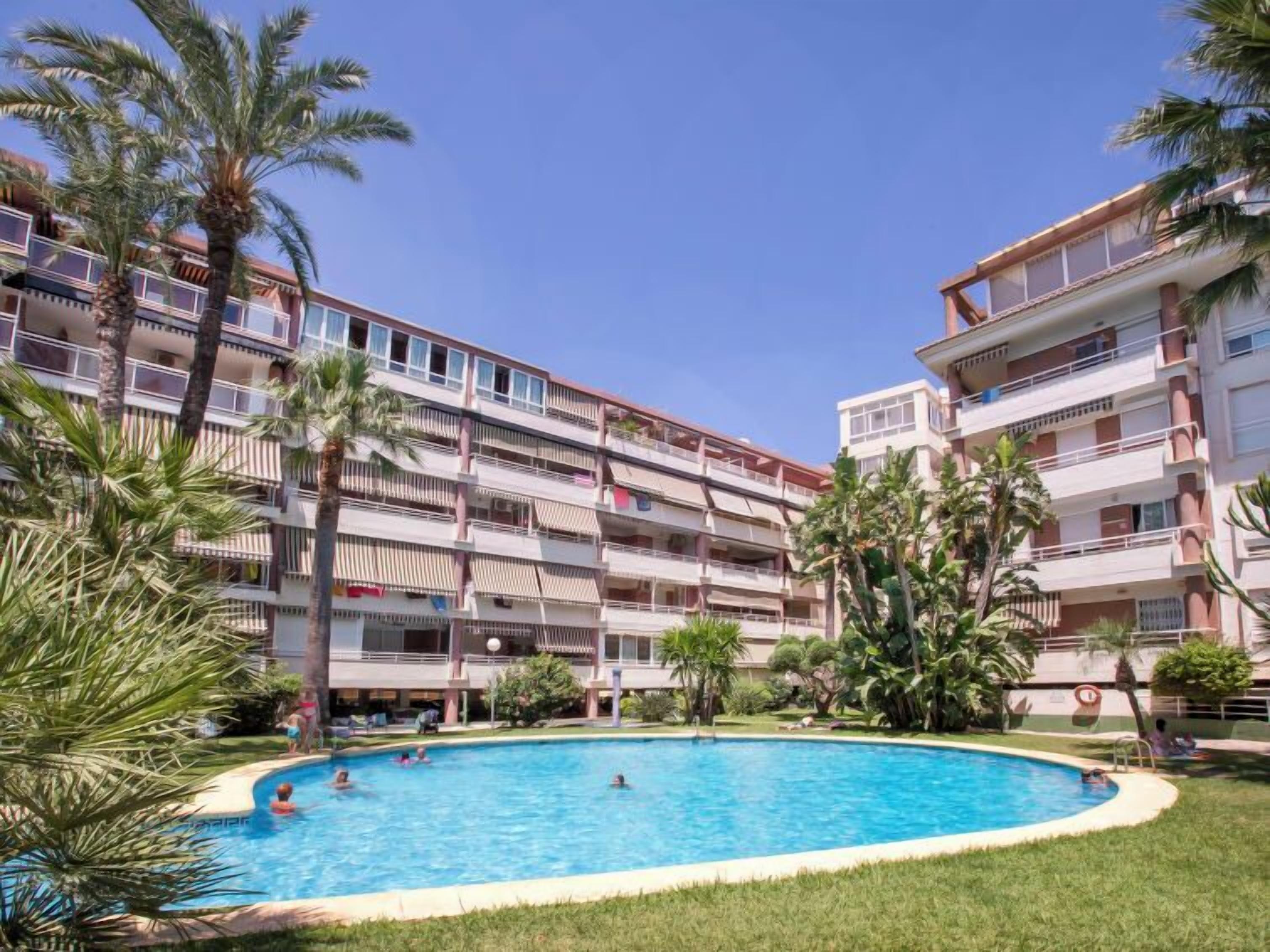 A multi-story hotel with a swimming pool surrounded by palm trees and greenery.