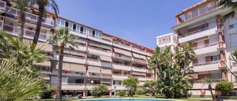 A multi-story hotel with a swimming pool surrounded by palm trees and greenery.