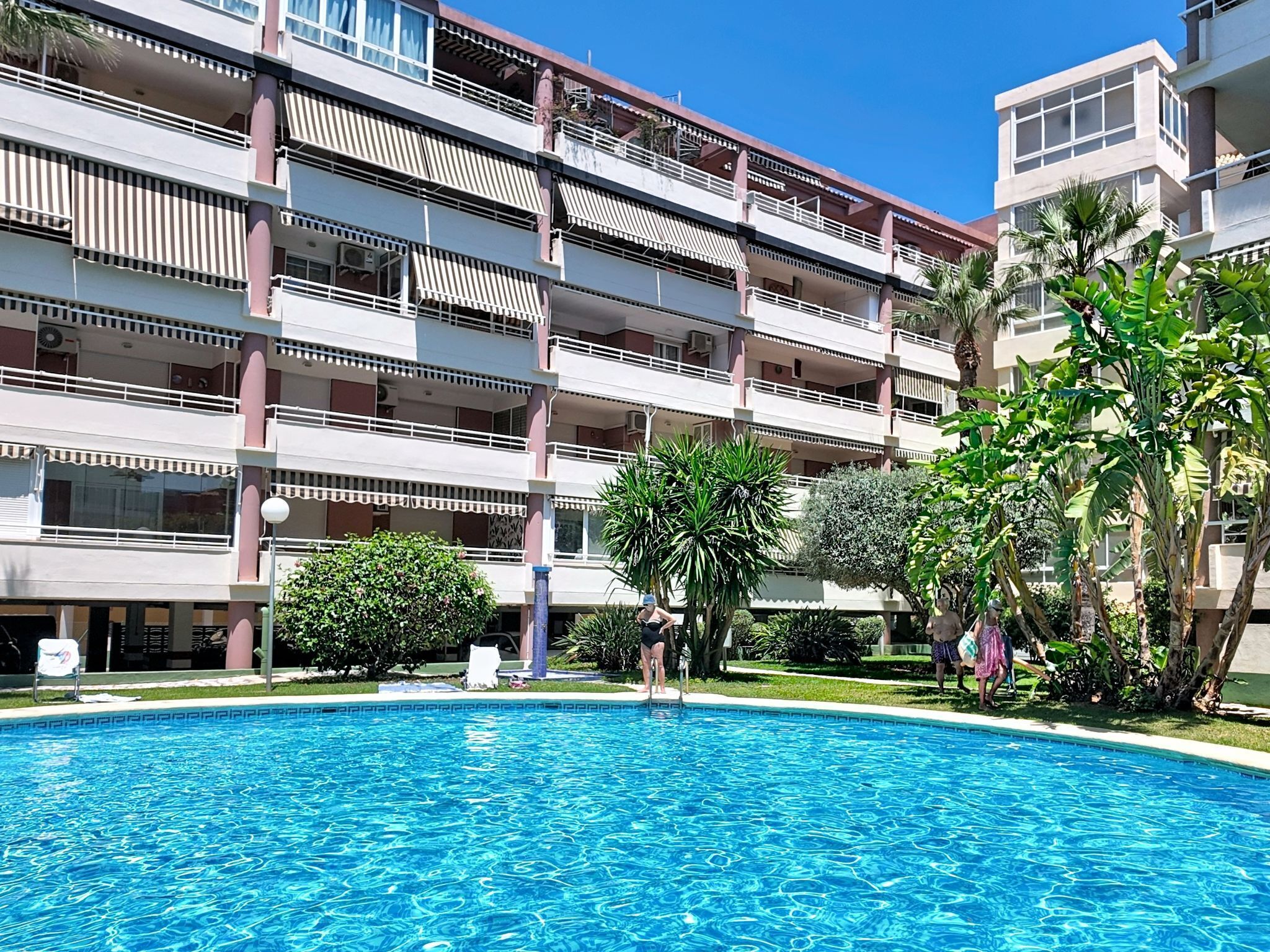 A multi-story hotel with a swimming pool, balconies, and greenery.