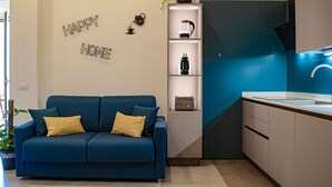 A modern living room with a blue sofa, a coffee machine, and a shelf with decorative items. - Lele Rooms Termini (Rome)