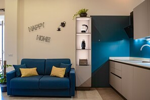 Un soggiorno moderno con un divano blu, una macchina da caffè e uno scaffale con oggetti decorativi.