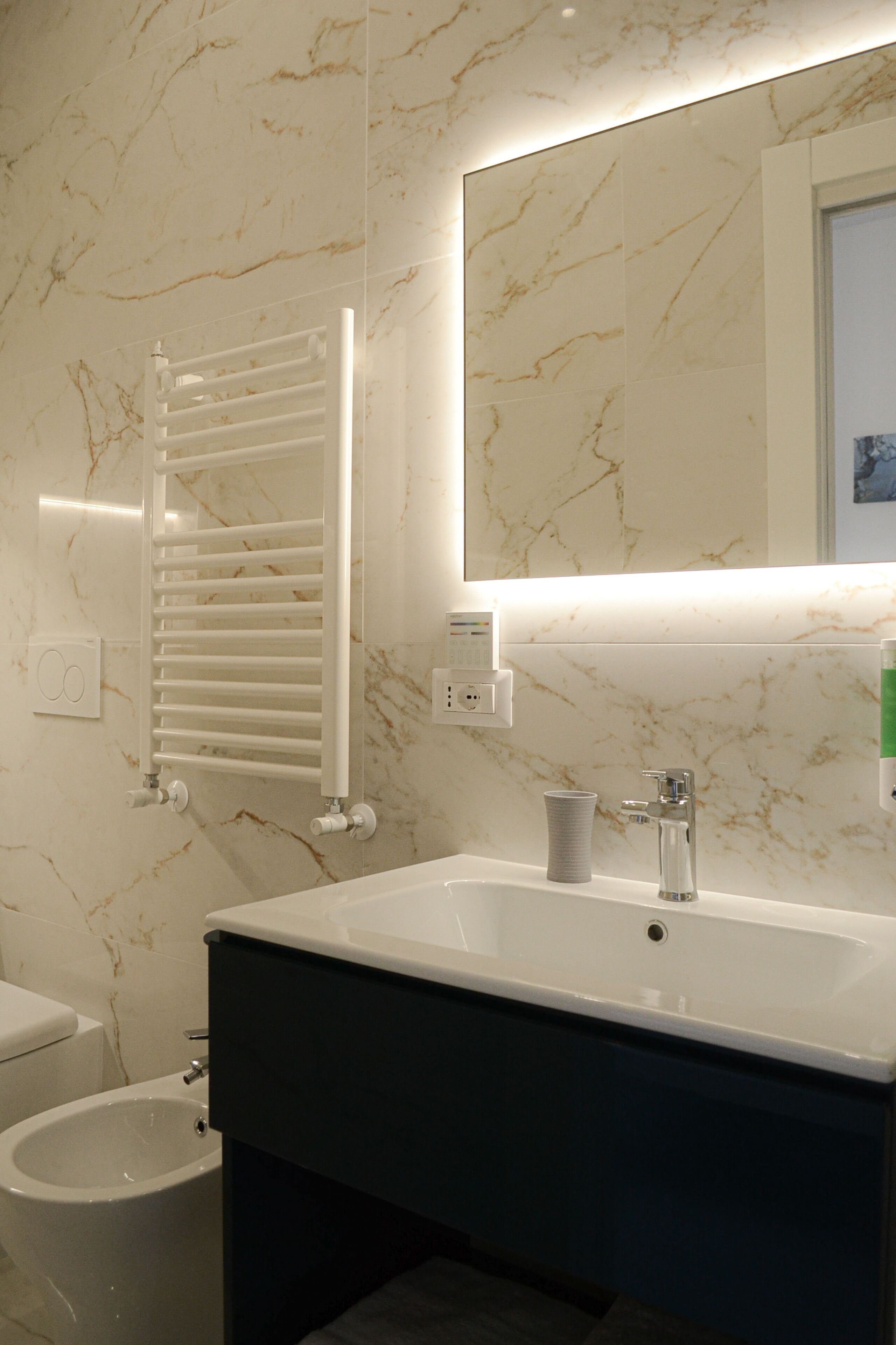 A modern bathroom with a marble wall, a white sink, and a bidet.