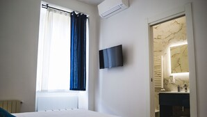 A bedroom with a bed, a window with curtains, a mounted TV, and a bathroom with a marble wall and towel rack. - Lele Rooms Termini (Rome)
