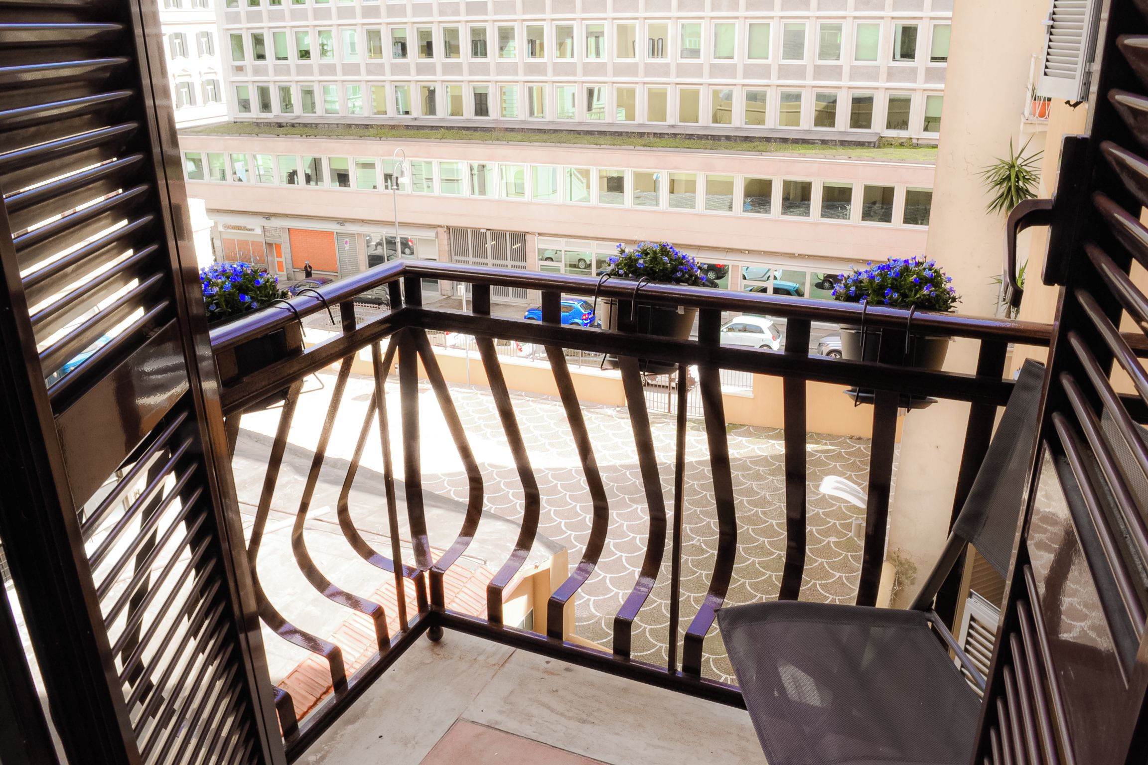 Un balcon avec une rambarde en métal, des plantes en pot et une vue sur un parking et des immeubles.