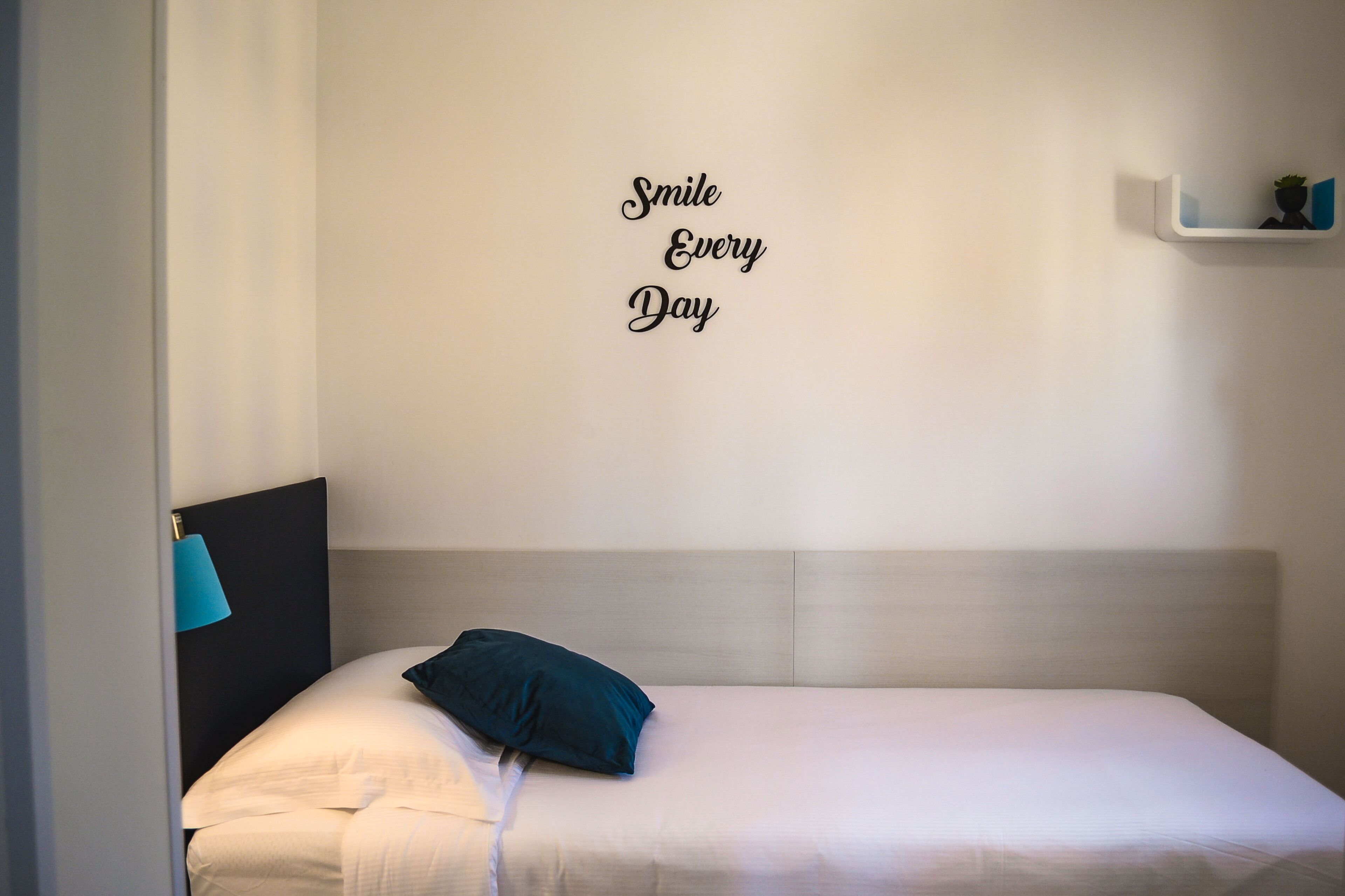 A bedroom with a bed, a wall-mounted shelf with a plant, and a motivational quote.