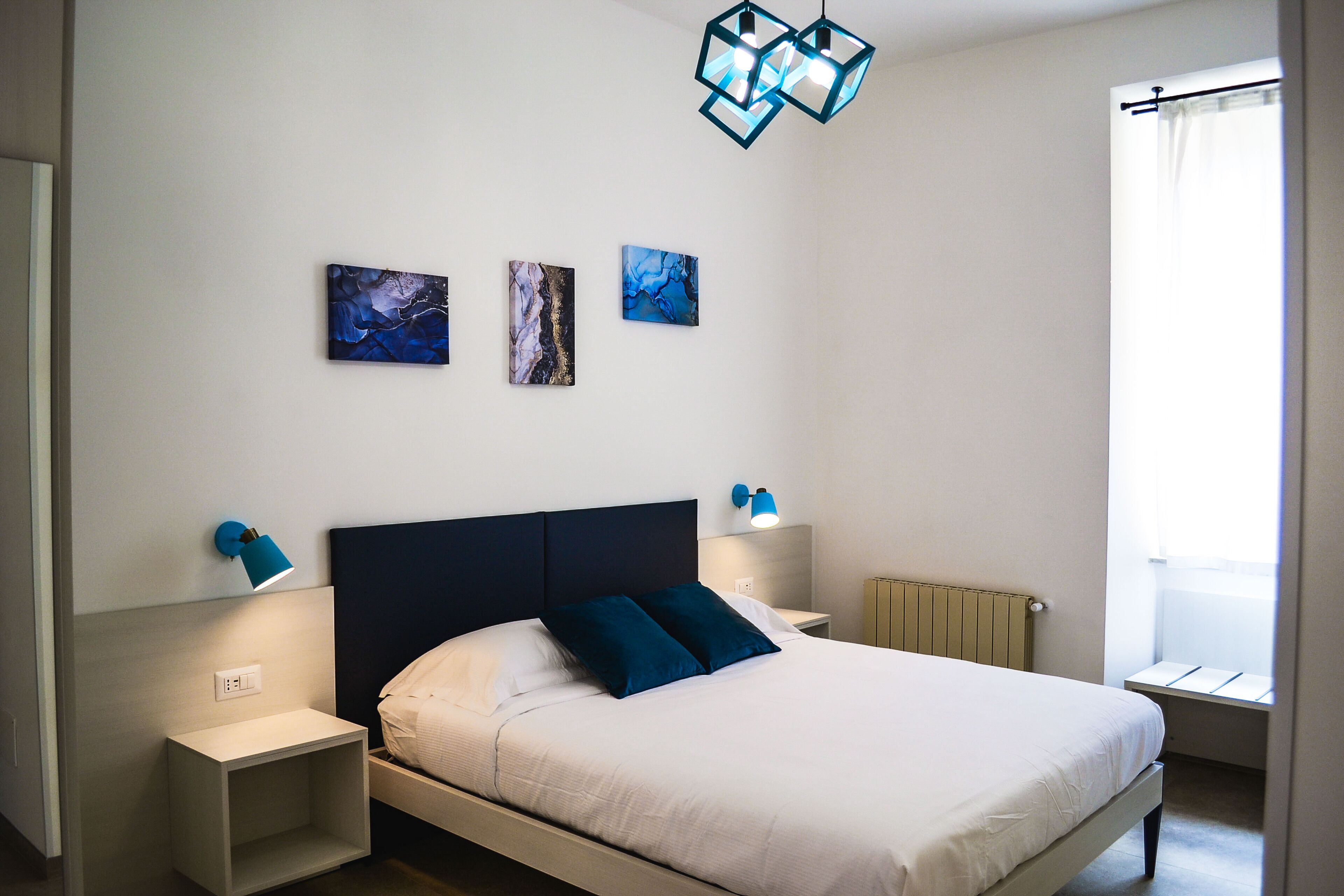 Une chambre à coucher avec un lit, des lampes de chevet, un radiateur et des œuvres d’art accrochées au mur.