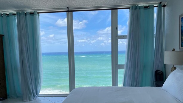 Ein Hotelzimmer mit einem großen Bett, Meerblick und hellblauen Vorhängen.