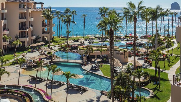 A resort with a large swimming pool, palm trees, and a view of the ocean.