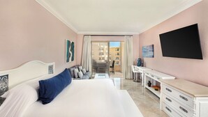 A hotel room with a large bed, a desk, a flat-screen TV, and a view of the outside balcony.