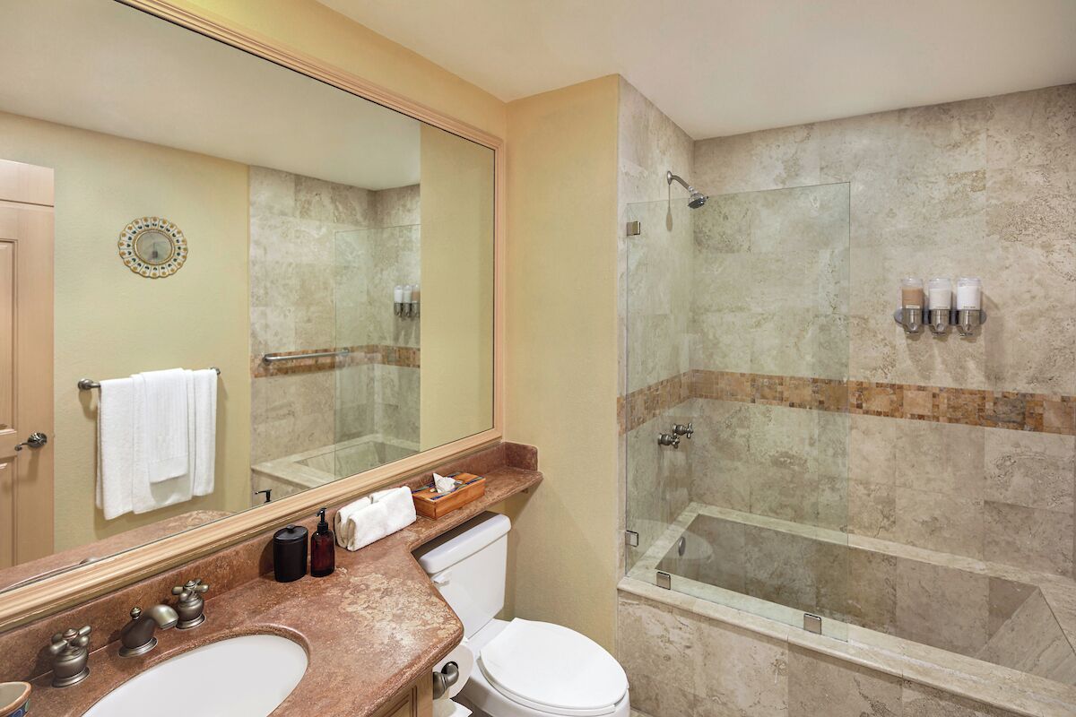 A bathroom with a large mirror, two sinks, a toilet, and a glass-enclosed shower area.