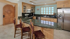 A kitchen with a marble countertop, wooden cabinets, a stainless steel refrigerator, and a large window.