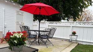 Un patio con una mesa y sillas de metal, una sombrilla roja y una pequeña mesa con flores.