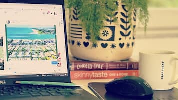 Una computadora portátil mostrando un mapa, un ratón, una taza de café, una planta en maceta y libros sobre un escritorio.