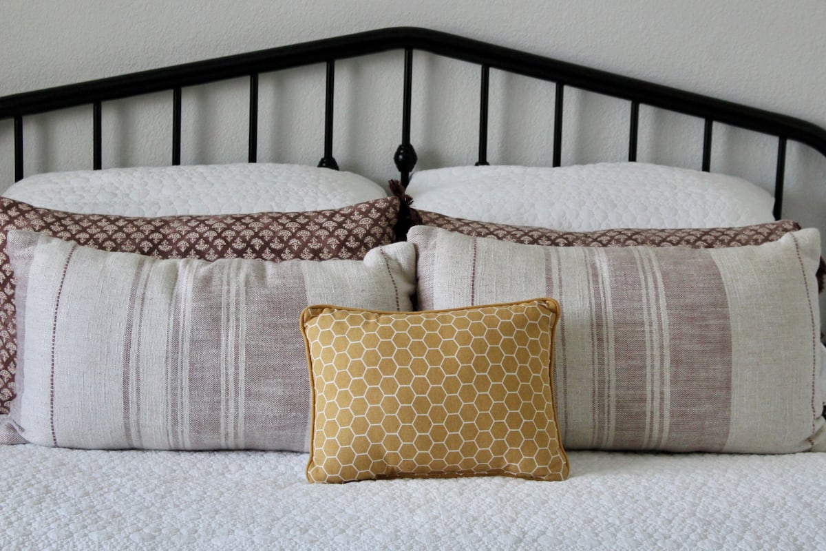 Ein Bett mit schwarzem Metallkopfteil, zwei Kissen mit Streifenmuster und ein Kissen mit geometrischem Muster.