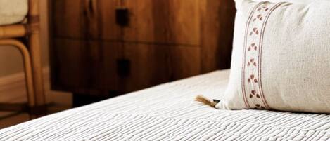 Ein Bett mit cremefarbener, strukturierter Bettdecke und einem Zierkissen mit Quaste.