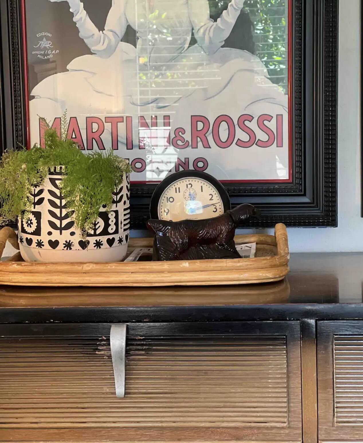 A decorative tray with a clock and a plant on a wooden surface.