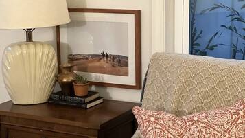 A room with a wooden nightstand, a lamp, a framed picture, a patterned sofa, and a window with a bamboo view.
