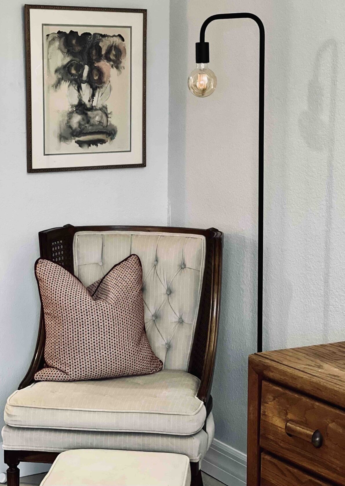 A chair with a patterned cushion, a framed artwork above it, and a modern light fixture on the wall.