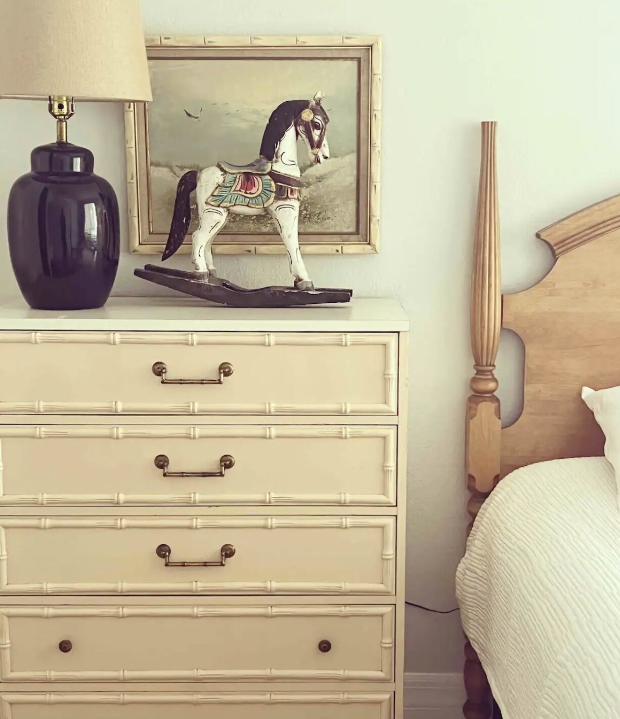 Une chambre à coucher avec un lit, une commode à tiroirs, une lampe et un tableau représentant un cheval.