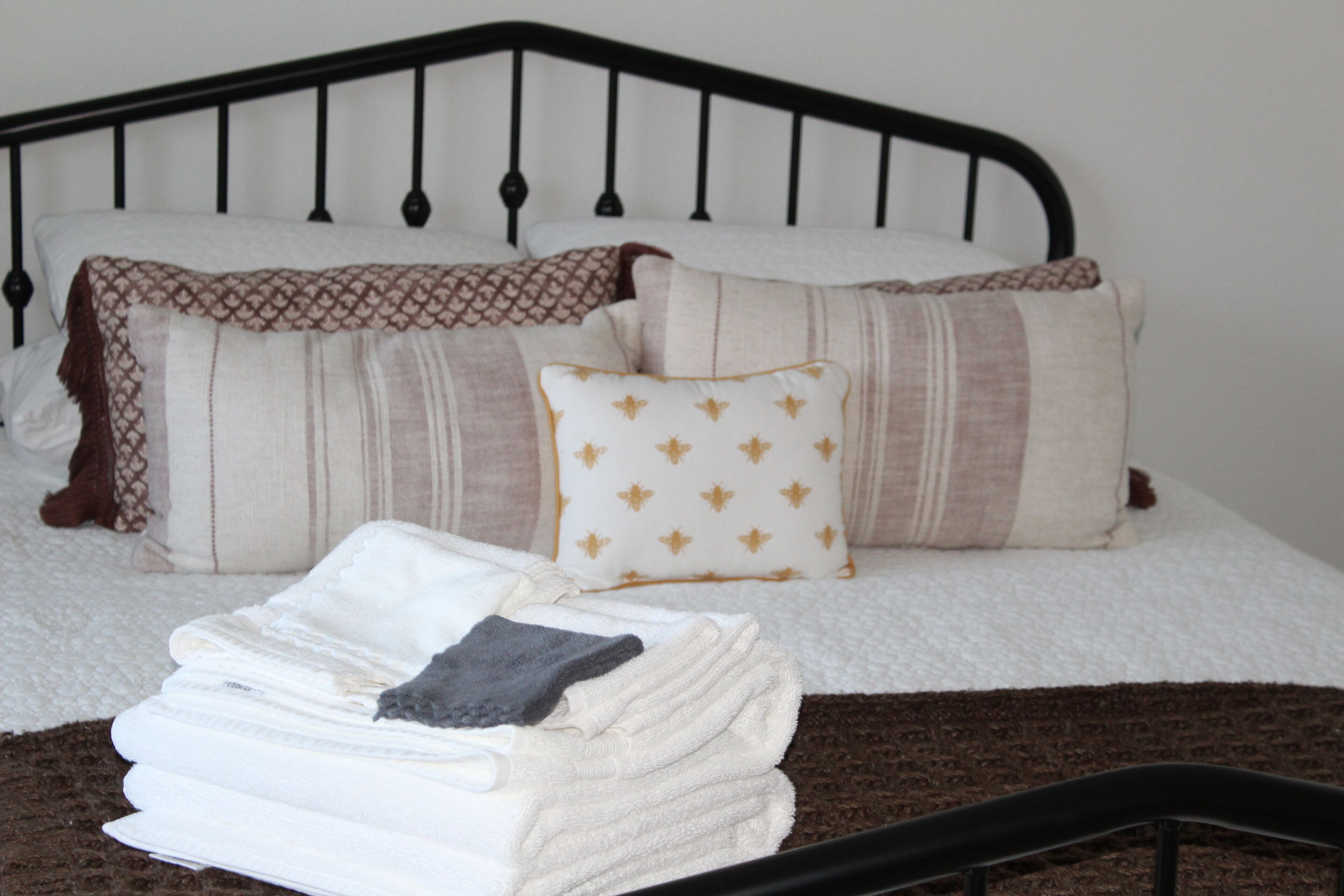 A neatly made bed with a black metal headboard, multiple pillows, and a stack of folded towels.