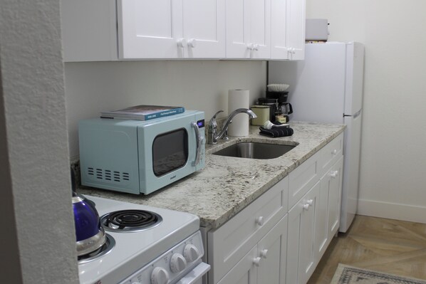 A compact kitchen with white cabinets, a microwave, a stove, and a sink.