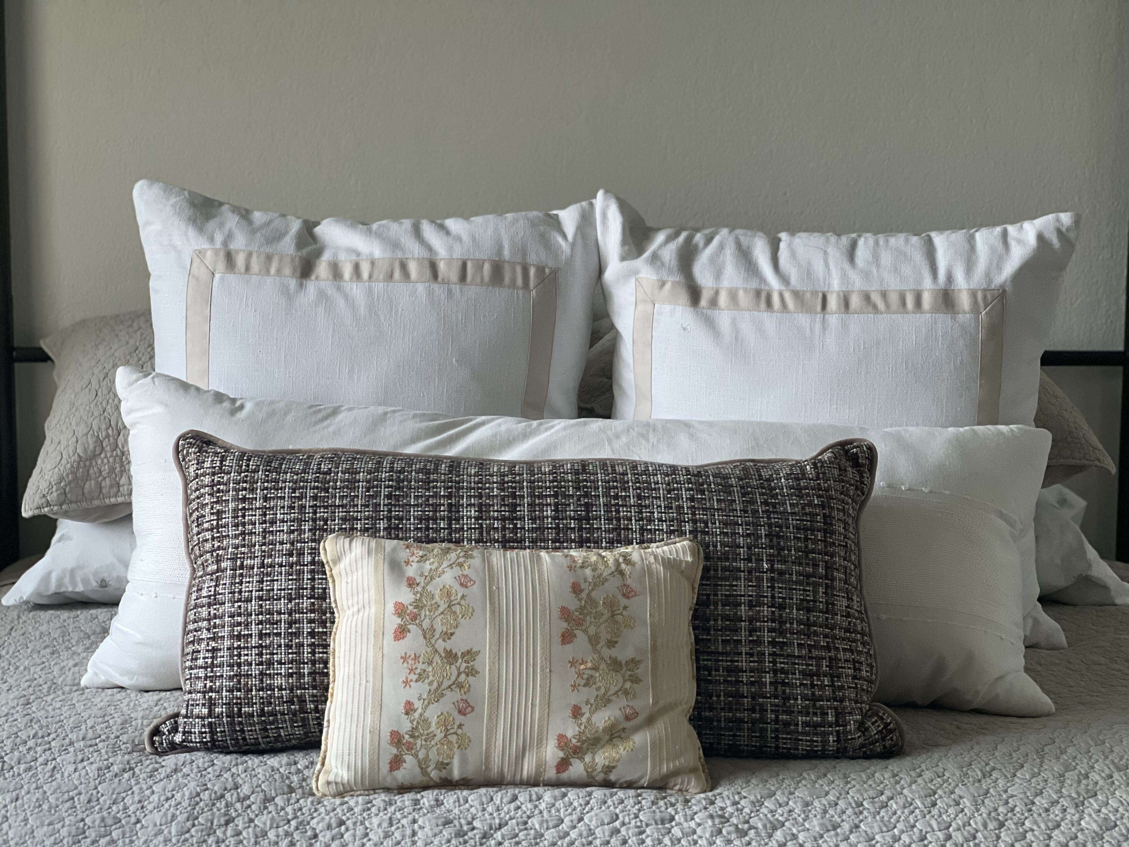 Una cama ordenada con varios almohadones, incluyendo un cojín decorativo con motivos florales y uno con textura.