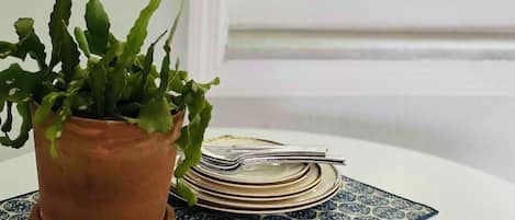 Una planta en maceta sobre un mantel estampado, con platos apilados y un tenedor.