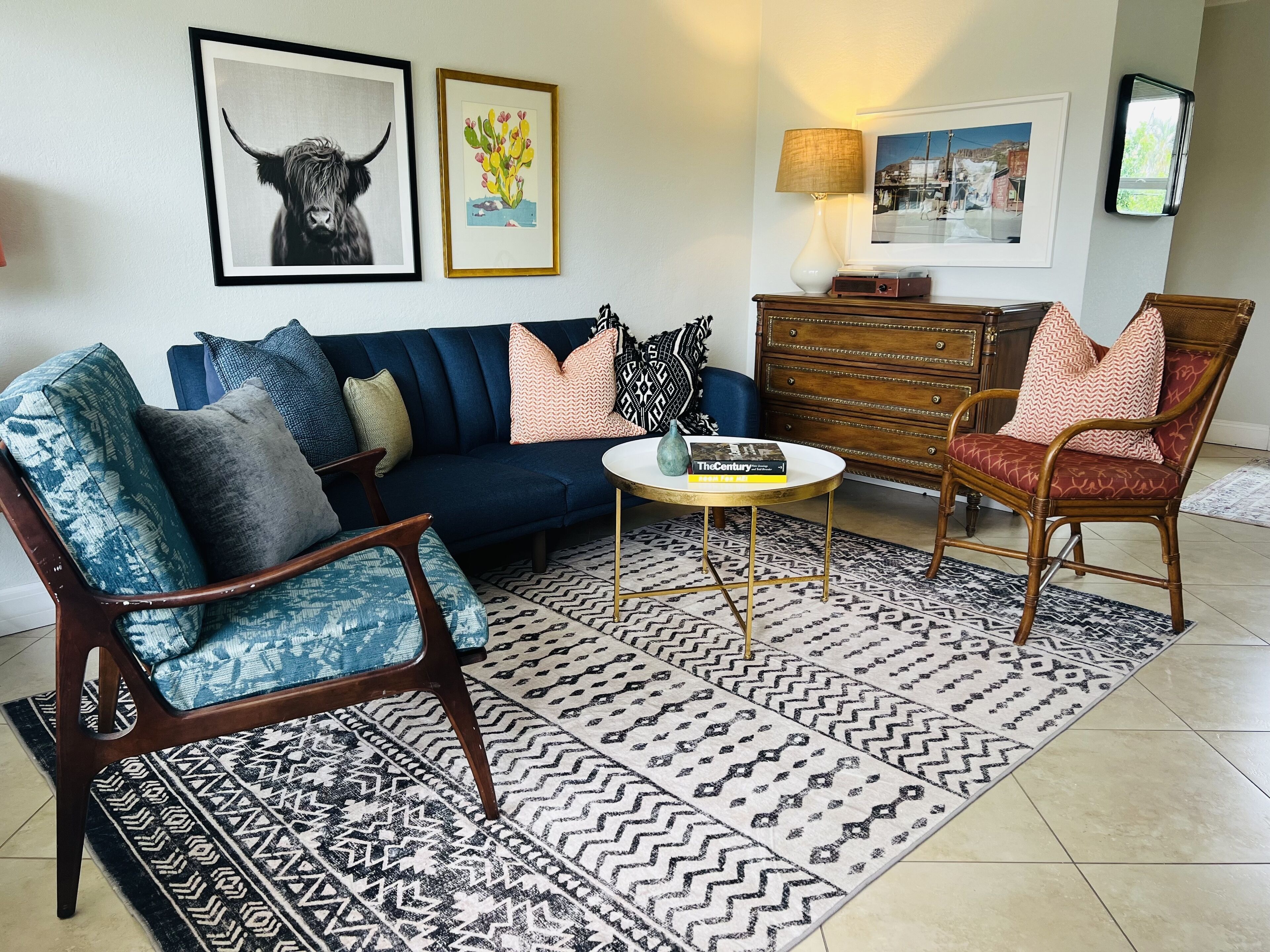 A living room with a dark blue sofa, patterned armchairs, a coffee table, and a patterned rug.