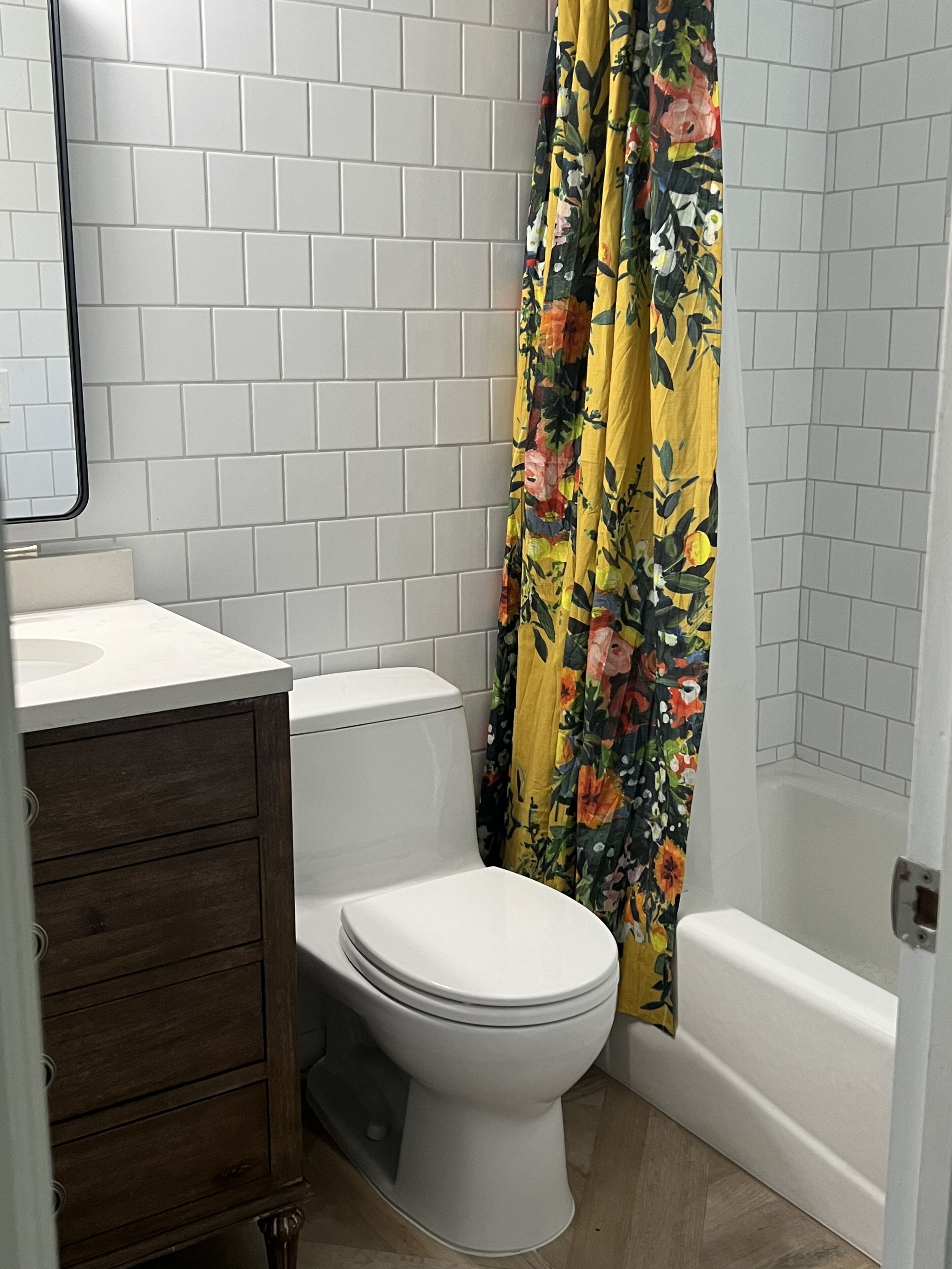 Un baño con inodoro, lavamanos, un mueble de madera y cortina de ducha.