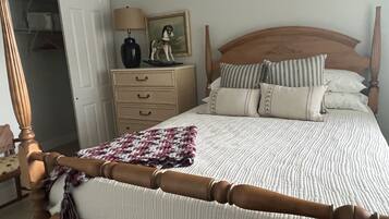 A neatly made bed with a wooden headboard, a bedside table with a lamp and a small statue, and a wardrobe in the background.