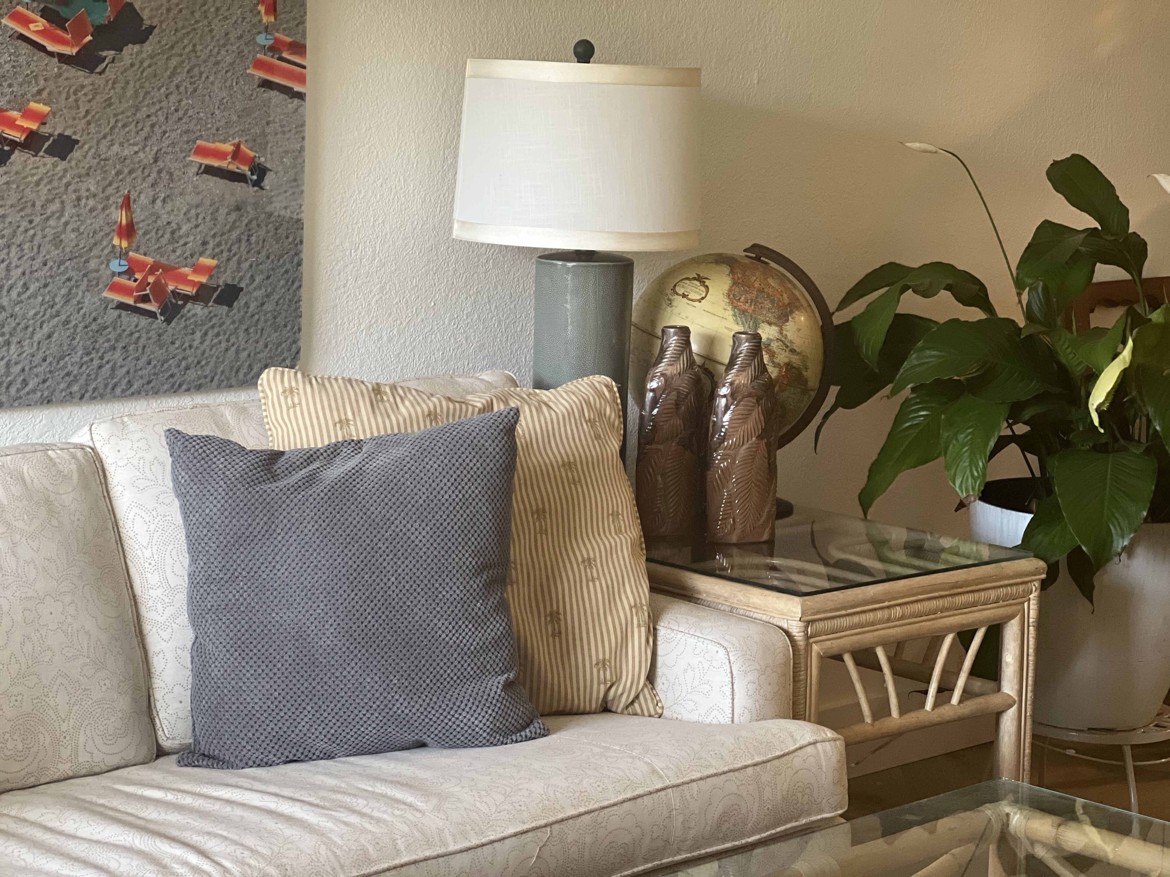 Un salon avec un canapé, des coussins, une lampe, un globe terrestre et une plante.