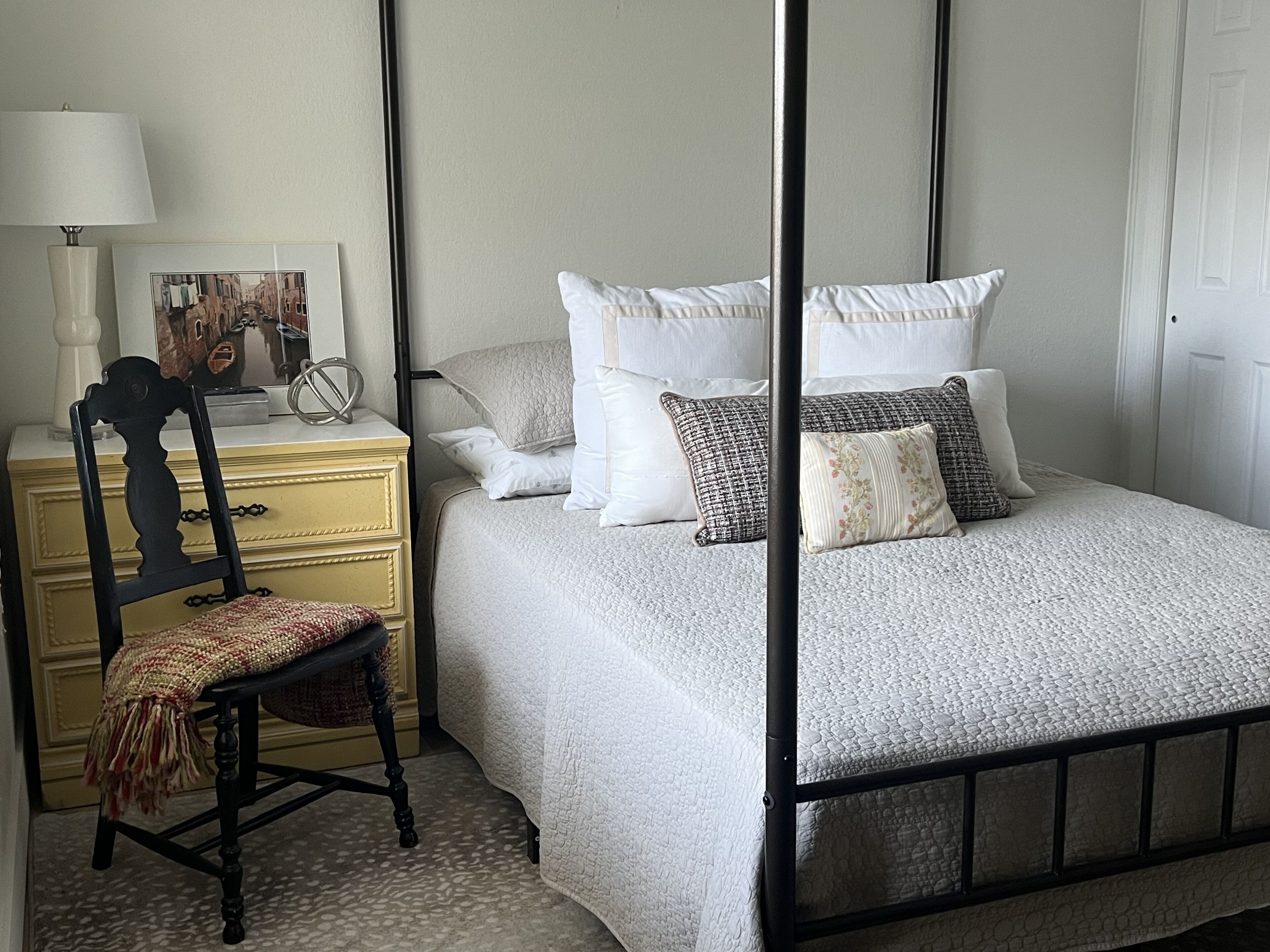 Une chambre à coucher bien aménagée, avec un lit à baldaquin, une table de chevet avec une lampe et un fauteuil agrémenté d’un plaid.