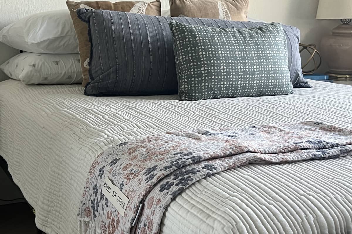 Ein Bett mit weißer gesteppter Bettdecke, einer gemusterten Tagesdecke und mehreren Kissen in verschiedenen Farben und Mustern.