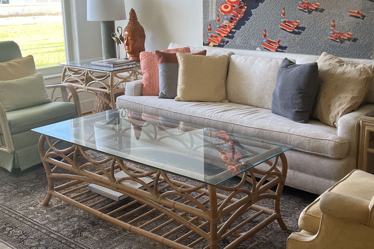 Ein Wohnzimmer mit Glastisch, Korbmöbeln, einem gemusterten Sofa und einer dekorativen Wandmalerei.